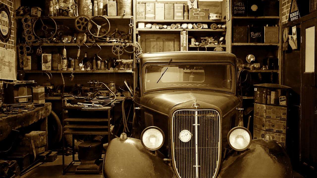 services-01 A vintage car surrounded by antique tools and parts in a nostalgic workshop.
