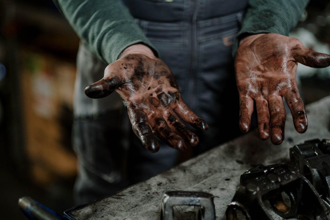 services-06 Close-up of a mechanic's dirty hands in a garage workspace with grease and spare parts.